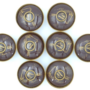 May include: Set of eight small, round, brown bowls with gold painted designs. Each bowl features a mountain scene with a bridge and trees. The bowls are arranged in a circle.