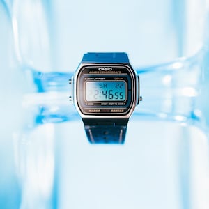 May include: A digital Casio watch with a black strap and a blue top. The watch face displays the time, date, and other functions. The watch has the text "CASIO ALARM CHRONOGRAPH" and "WATER RESIST" printed on it.