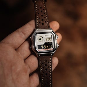 May include: A silver digital watch with a brown leather strap. The watch face shows the time as 4:55:50 and the text "REMOVE BEFORE FLIGHT". The strap has a perforated design.