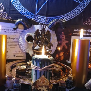 May include: A gold metal tray with candles, a small statue of a demon, and various bottles and jars. The tray is on a dark surface with a black and blue patterned fabric in the background. The text on the certificate reads "Internationally Certified Vodou Theology Master Class".