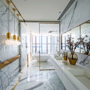 May include: A modern bathroom with white marble walls and floors, a freestanding bathtub, and a double vanity with a white countertop. The bathroom has a large window with a view of the city.
