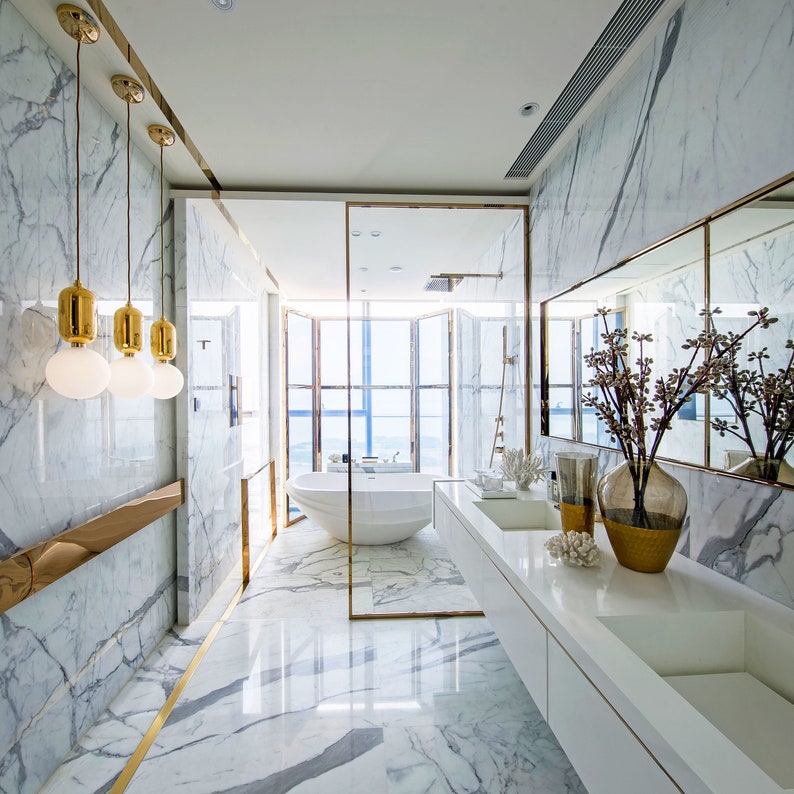 May include: A modern bathroom with white marble walls and floors, a freestanding bathtub, and a double vanity with a white countertop. The bathroom has a large window with a view of the city.