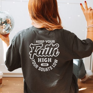 May include: A dark gray t-shirt with the text "Keep your Faith High and your Squats Low" printed on the back in white.