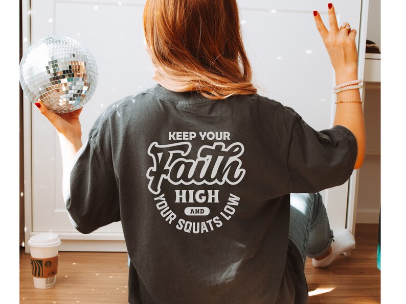 May include: A dark gray t-shirt with the text "Keep your Faith High and your Squats Low" printed on the back in white.