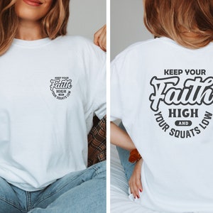 May include: White t-shirt with a black graphic print on the front and back. The graphic says "Keep Your Faith High And Your Squats Low".