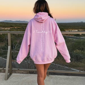 May include: A pink hoodie with the text "2 Timothy 1:7" and the phrase "for God gave us a spirit not of fear but of power and love and self-control" printed vertically down the back.
