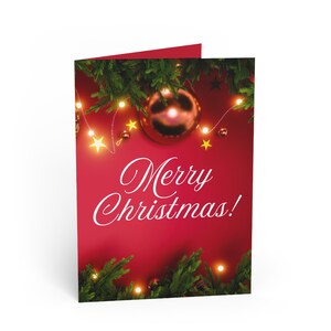 May include: A folded Christmas card with a red background and the words "Merry Christmas!" in white script. The card is decorated with green pine branches, gold baubles, and fairy lights.