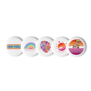Könnte beinhalten: Fünf weiße, runde Buttons mit farbenfrohen Designs. Ein Button zeigt den Text "BE YOU" in Regenbogenfarben. Ein weiterer Button zeigt einen Regenbogen und den Text "GENDER IS A SPECTRUM". Weitere Buttons zeigen Illustrationen von Gesichtern, Planeten und einer lesbischen Pride-Flagge.
