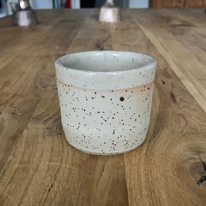 Könnte beinhalten: Eine weiße Keramiktasse mit braunen Flecken. Die Tasse hat eine leicht abgerundete Form und eine glatte, glasierte Oberfläche.