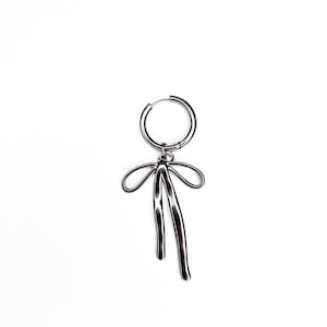May include: Silver hoop earring with a dangling bow charm. The bow is made of textured metal and has a slightly asymmetrical shape.