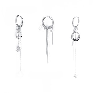 Puede incluir: Tres pendientes plateados con diferentes diseños. Uno tiene una espiral y cadena, otro múltiples cadenas y cuentas transparentes, y el tercero un dije de estrella. Todos los pendientes tienen un diseño de aro.