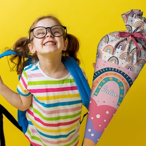 May include: A cone-shaped gift bag featuring a colorful rainbow pattern, pink accents, and white polka dots. The name Julia is printed in white script on the front. The top is gathered and tied with a dark pink ribbon, creating a festive presentation.