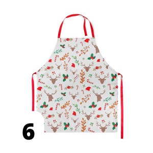 Pu&ograve; includere: Un grembiule da cucina rosso e bianco a tema natalizio con un motivo di renne, bastoncini di zucchero, agrifoglio e alberi di Natale.