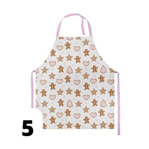 Pu&ograve; includere: Un grembiule da cucina rosa e bianco con un motivo a biscotti di pan di zenzero. Il grembiule ha una fettuccia regolabile rosa per il collo e due lacci rosa.