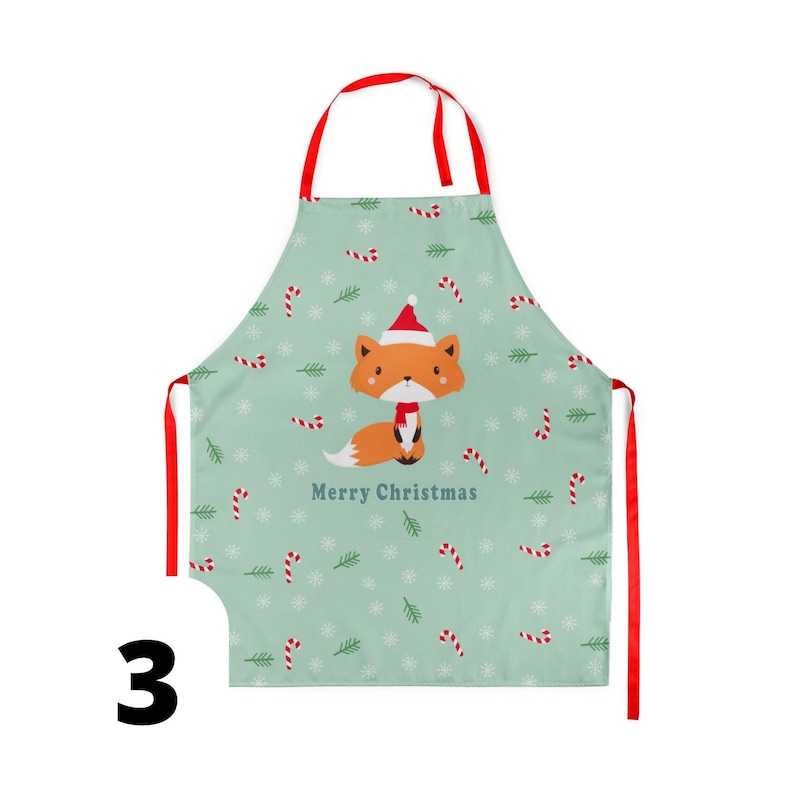 Pu&ograve; includere: Un grembiule verde a tema natalizio con una volpe rossa che indossa un cappello da Babbo Natale e il testo "Merry Christmas". Il grembiule ha un laccio di nastro rosso.