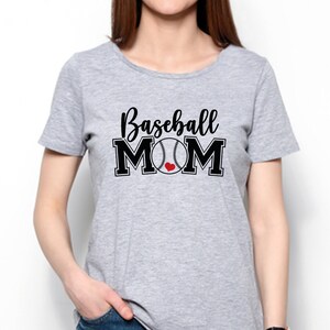 May include: A light gray t-shirt with the words "Baseball MOM" in black script and block letters. A baseball graphic with a red heart replaces the "O" in MOM. The shirt is short-sleeved.