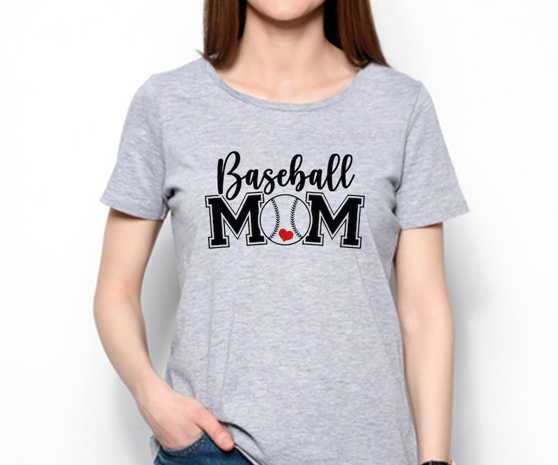 May include: A light gray t-shirt with the words "Baseball MOM" in black script and block letters. A baseball graphic with a red heart replaces the "O" in MOM. The shirt is short-sleeved.