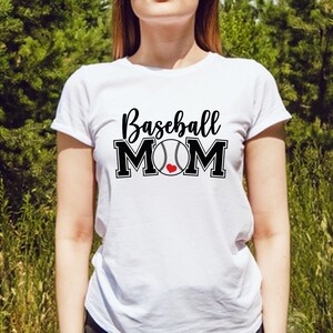 May include: White t-shirt with the text "Baseball MOM" in black script and block letters. The baseball graphic has a red heart in the center. The shirt is a crew neck style.