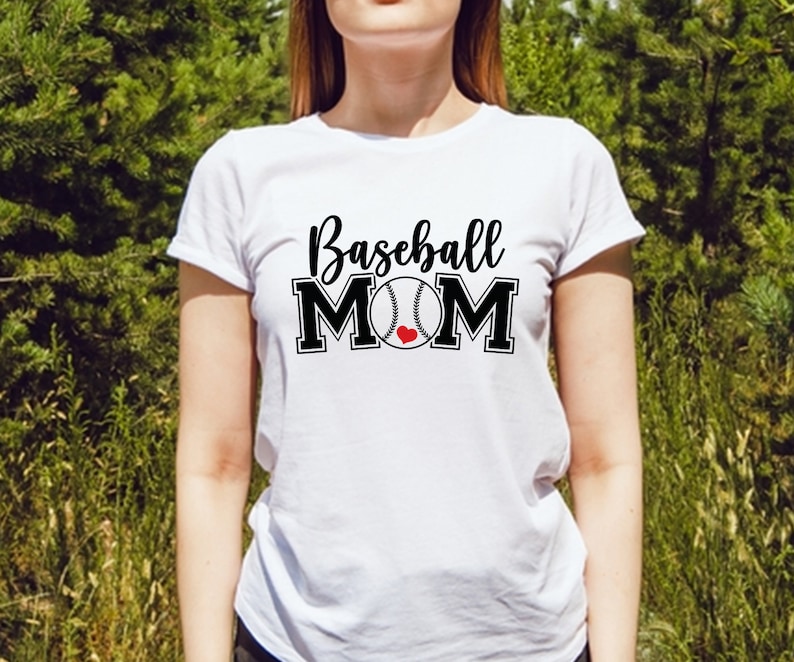 May include: White t-shirt with the text "Baseball MOM" in black script and block letters. The baseball graphic has a red heart in the center. The shirt is a crew neck style.