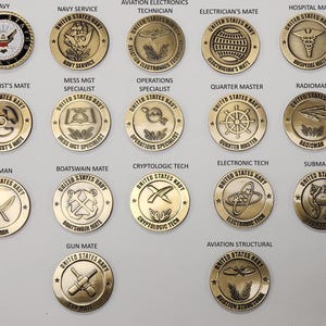May include: A collection of 16 gold-colored United States Navy rate badges. Each badge features a different design and the words "United States Navy" around the edge.