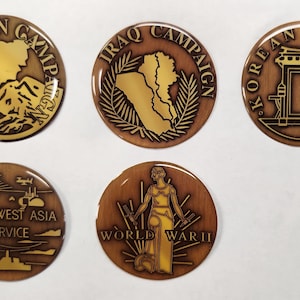 May include: A collection of five round, bronze-colored military campaign pins. Each pin features a different design and text, including "AFGHANISTAN CAMPAIGN", "IRAQ CAMPAIGN", "KOREAN SERVICE", "SOUTHWEST ASIA SERVICE", and "WORLD WAR II".