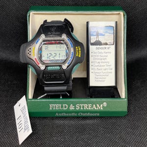K&ouml;nnte beinhalten: Eine schwarze Field & Stream Sensor III Uhr mit Digitalanzeige, in der originalen gr&uuml;nen Box. Die Uhr hat ein schwarzes Armband, gr&uuml;ne Akzente und den Text "WATER RESIST". Ein Etikett mit "F101" ist an der Box befestigt.