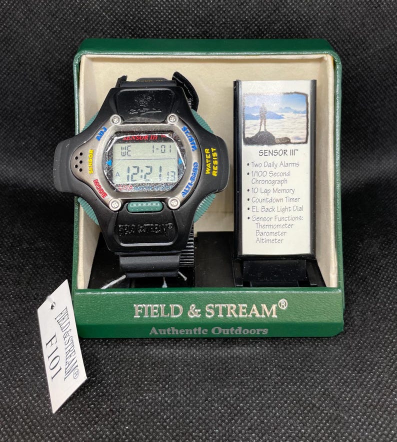 K&ouml;nnte beinhalten: Eine schwarze Field & Stream Sensor III Uhr mit Digitalanzeige, in der originalen gr&uuml;nen Box. Die Uhr hat ein schwarzes Armband, gr&uuml;ne Akzente und den Text "WATER RESIST". Ein Etikett mit "F101" ist an der Box befestigt.
