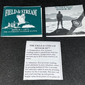 K&ouml;nnte beinhalten: Drei bedruckte Karten. Eine ist t&uuml;rkis und tr&auml;gt die Aufschrift "FIELD & STREAM" und "SINCE 1871 THE AUTHENTIC OUTDOOR WATCH". Eine andere zeigt eine Uhr und eine Person auf einem Berg. Die dritte Karte enth&auml;lt Anweisungen f&uuml;r die Uhr "SENSOR III".