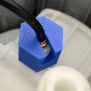 Puede incluir: Primer plano de una abrazadera de alambre hexagonal azul impresa en 3D. La abrazadera sujeta un cable negro en su lugar.