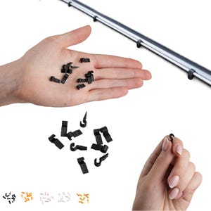 Puede incluir: Una colección de pequeños clips de plástico negro diseñados para la gestión de cables. Estos clips cuentan con un gancho en forma de C y una base plana, mostrados en varias orientaciones. El conjunto incluye varias piezas individuales.