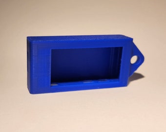 Pode incluir: Uma pequena caixa de plástico azul com uma abertura retangular e um laço no lado. A caixa é projetada para conter um pequeno dispositivo eletrônico.