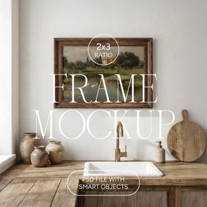 Pode incluir: Uma pintura de paisagem emoldurada com uma moldura de madeira escura está pendurada acima de uma pia de cozinha. O texto "FRAME MOCKUP" é sobreposto na imagem. A cozinha apresenta uma bancada de madeira, uma torneira dourada e cerâmica decorativa.