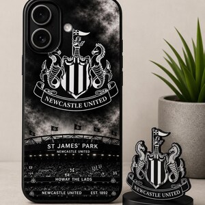 May include: Black phone case and desk ornament featuring the Newcastle United crest. The phone case displays the team's logo, stadium, and text. The desk ornament is a miniature version of the crest. The text includes "ST JAMES' PARK", "HOWAY THE LADS", and "EST. 1892".