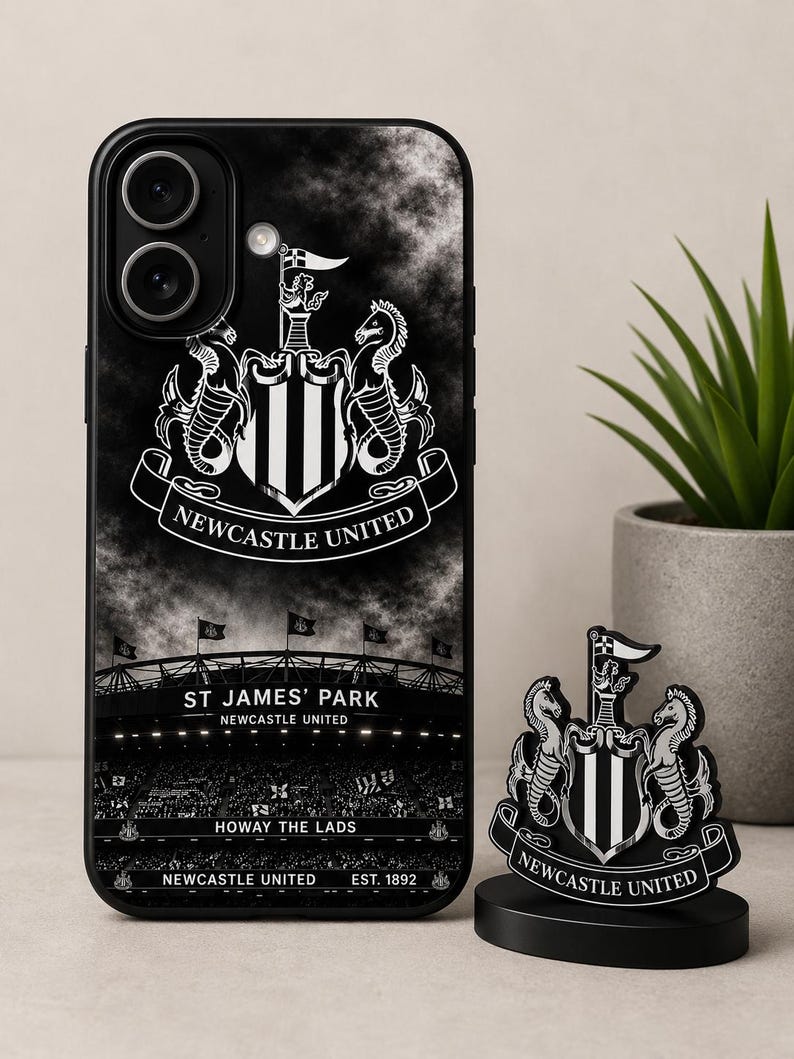 May include: Black phone case and desk ornament featuring the Newcastle United crest. The phone case displays the team's logo, stadium, and text. The desk ornament is a miniature version of the crest. The text includes "ST JAMES' PARK", "HOWAY THE LADS", and "EST. 1892".