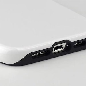 May include: Close-up of a white phone case with a black accent around the charging port and speaker holes. The case has a glossy finish and a smooth, curved design. The charging port is visible.