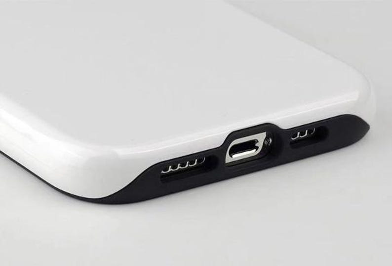 May include: Close-up of a white phone case with a black accent around the charging port and speaker holes. The case has a glossy finish and a smooth, curved design. The charging port is visible.