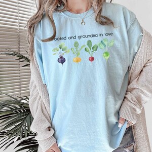 May include: A light blue t-shirt with the text "Rooted and grounded in love" and a row of five colorful cartoon vegetables.