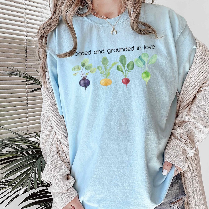 May include: A light blue t-shirt with the text "Rooted and grounded in love" and a row of five colorful cartoon vegetables.