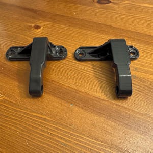 May include: Two black plastic door handles with a lever design. The handles are attached to a flat metal plate with two screws.