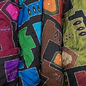 May include: Four fabric squares sewn together in a patchwork design. The squares are in shades of purple, blue, green, and brown. Each square has a different pattern of geometric shapes and floral designs. The fabric is decorated with sequins and embroidery.