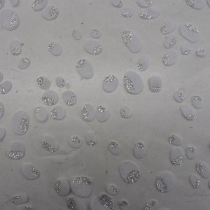 May include: White background with many small white circles with silver glitter on them.