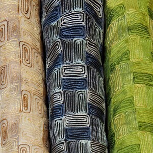 May include: Three fabric swatches with a geometric pattern of interlocking squares and rectangles. The swatches are beige, dark blue, and green.
