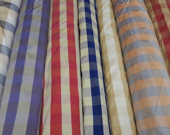 Op de afbeelding: Close-up van zes rollen stof met een geruit patroon. De stofrollen zijn in verschillende kleuren, waaronder beige, blauw, rood en oranje.