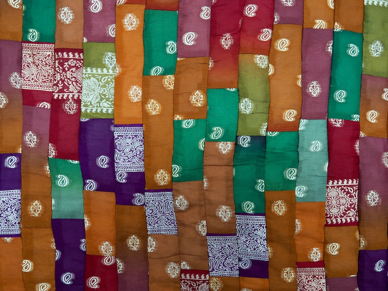 May include: A patchwork quilt made from a variety of fabrics in shades of red, green, purple, and brown. The fabric is patterned with paisley designs and white accents.