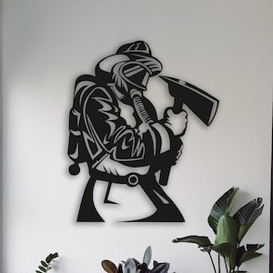 Puede incluir: Arte de pared de metal negro que representa a un bombero con casco y sosteniendo un hacha. El bombero lleva una máscara de gas y tiene un tanque en la espalda. El arte está montado en una pared blanca con plantas en macetas en primer plano.