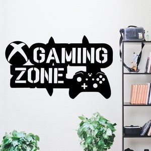 May include: Black and white wall decal with the text "Gaming Zone" and a stylized video game controller. The decal is on a white wall next to a black bookshelf with books and decorative items.