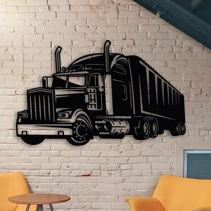 May include: A black metal wall art sculpture of a semi-truck with a trailer. The sculpture is mounted on a white brick wall. Two yellow chairs and a small table are in the foreground.
