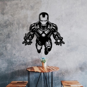May include: Black metal wall art depicting a superhero in flight. The art is displayed against a grey wall with a wooden table and chairs in the foreground.