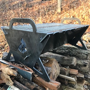 May include: A black metal grill with a triangular base and a handle. The grill is sitting on a pile of firewood.
