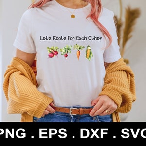 Op de afbeelding: Wit T-shirt met de tekst "Let's Roots For Each Other" en een afbeelding van verschillende groenten, waaronder wortels, radijsjes en maïs.